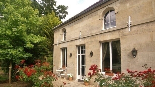 Un bâtiment en pierre doté d’un jardin, d’une terrasse avec des chaises et une table.