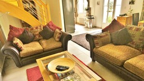 Un salon avec deux canapés, une table basse sur laquelle se trouve un magazine, et un escalier en arrière-plan.