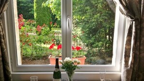 Une table à manger dressée avec des assiettes, des bols et des verres à vin, une bouteille de vin et un vase de fleurs posés sur un rebord de fenêtre.