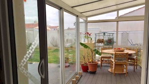 Une terrasse couverte avec une table et des chaises en bois, des plantes en pot et une vue sur le jardin arrière.