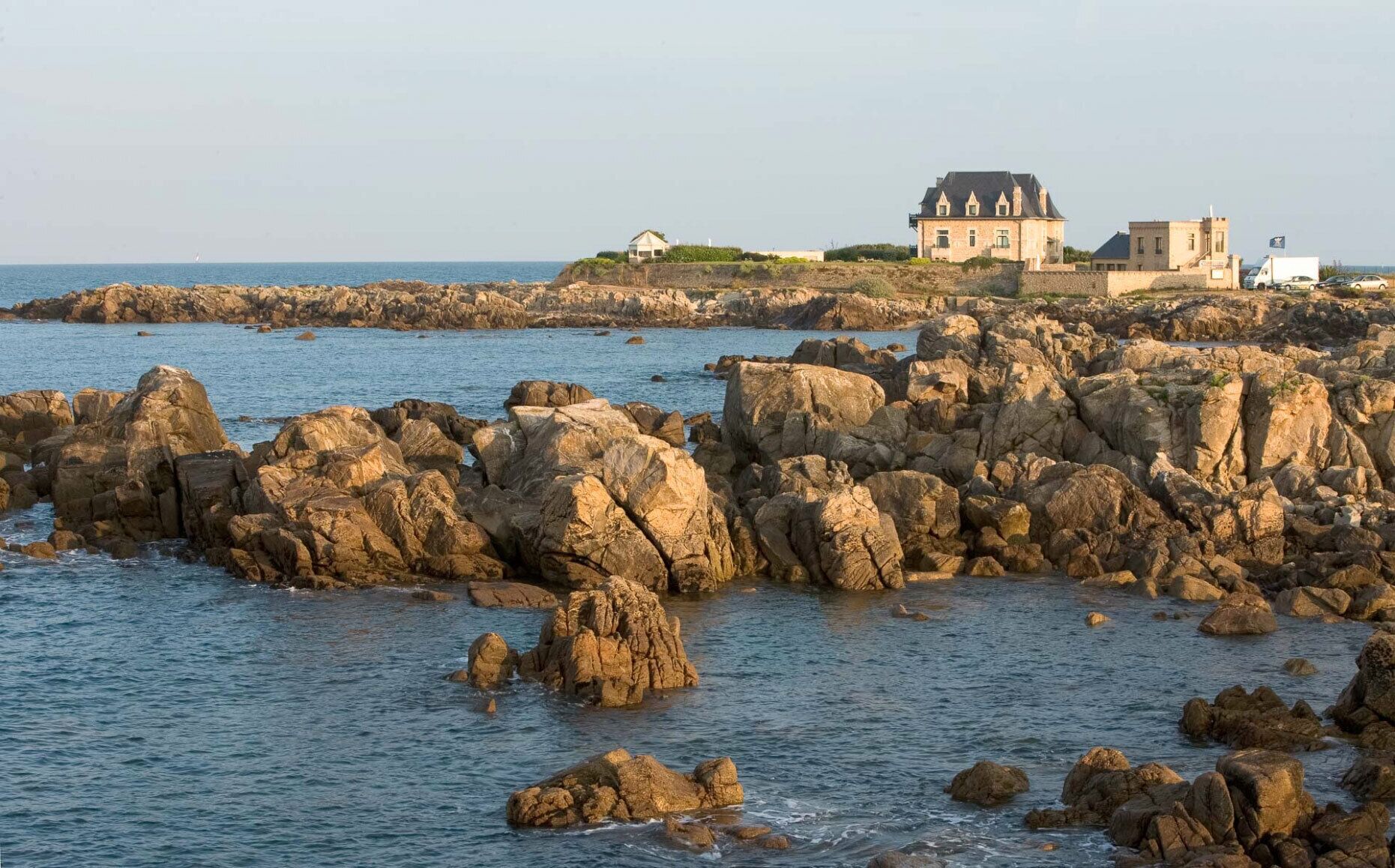 Une propriété située sur la côte, comprenant une grande maison et des bâtiments plus petits, le tout sur un littoral rocheux.