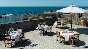Un área de comedor frente al mar, con mesas y sillas sobre una terraza de madera con vistas al océano.