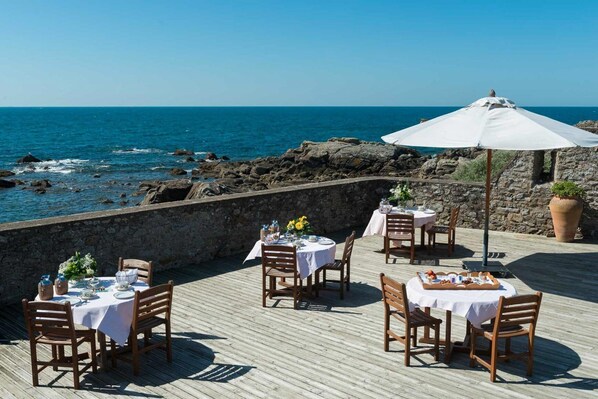 A seaside dining area with tables and chairs set up on a wooden deck overlooking the ocean. - Le Fort de l'Océan (Le Croisic)
