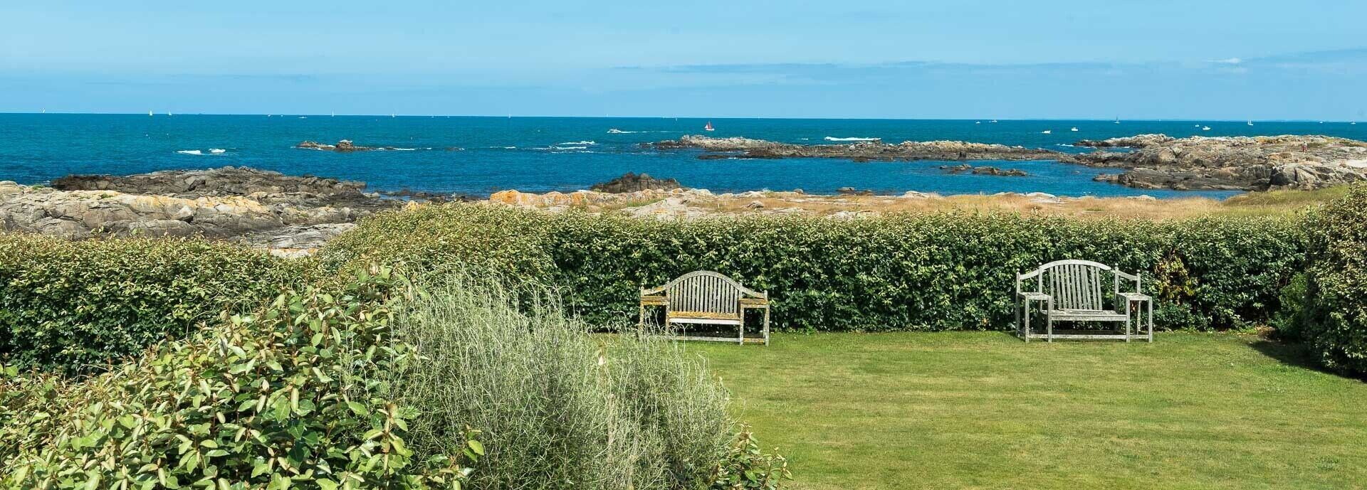 A view of a rocky coastline with two Adirondack chairs facing the sea.