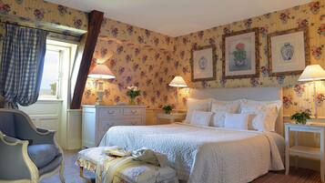 Une chambre à coucher avec un grand lit, deux tables de chevet avec des lampes, une chaise, une commode et un papier peint à motifs floraux.