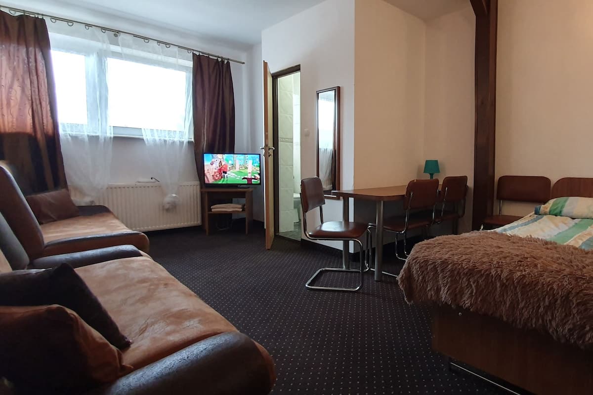 A hotel room with a bed, a desk with a chair, a television, and a window with curtains.
