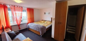 Ein Schlafzimmer mit einem Bett, einem Holzschrank, einem Schreibtisch mit Stuhl und einem Fenster mit Vorhängen.