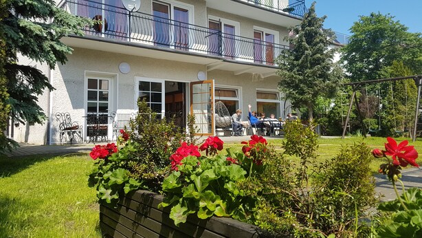 A multi-story hotel with balconies, outdoor seating, and a garden area with red flowers. - Dom Wczasowy Barbara (Wladyslawowo)