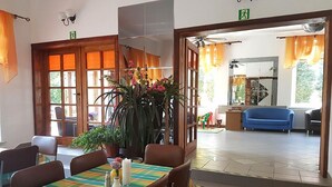 A dining area with a table set for two, a large potted plant, and a view of the living room through an open door. - Dom Wczasowy Barbara (Wladyslawowo)