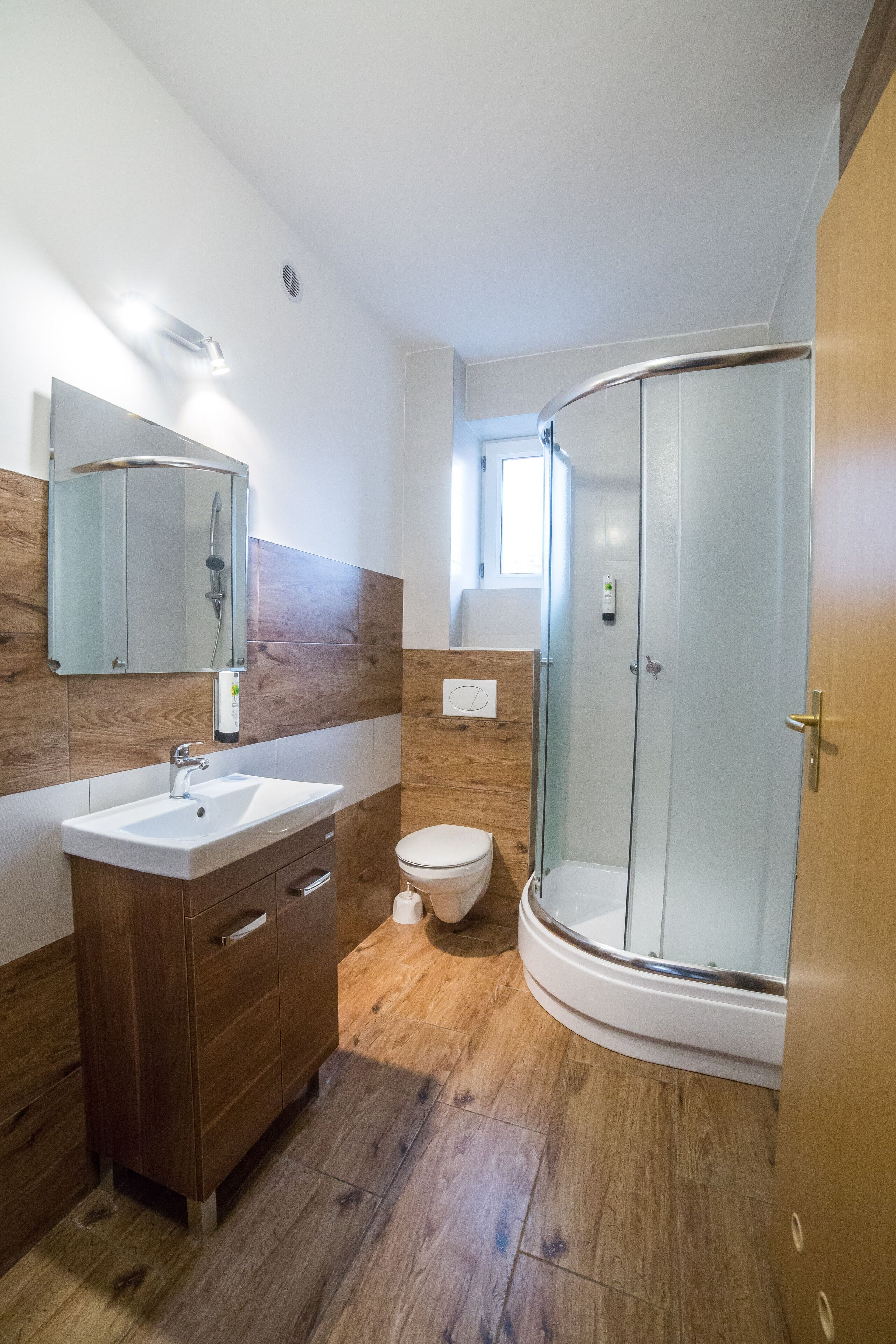 A modern bathroom with a wooden vanity, a glass shower enclosure, and a toilet.