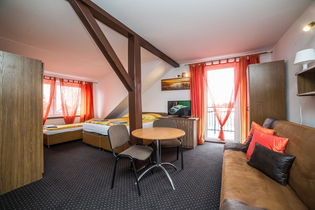 A room with a bed, a desk, a chair, a sofa, and a window with curtains.