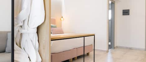 A modern hotel room with a wooden wardrobe, a bed with a wooden headboard, a small table with two wine glasses and cherries, and a minimalist design.