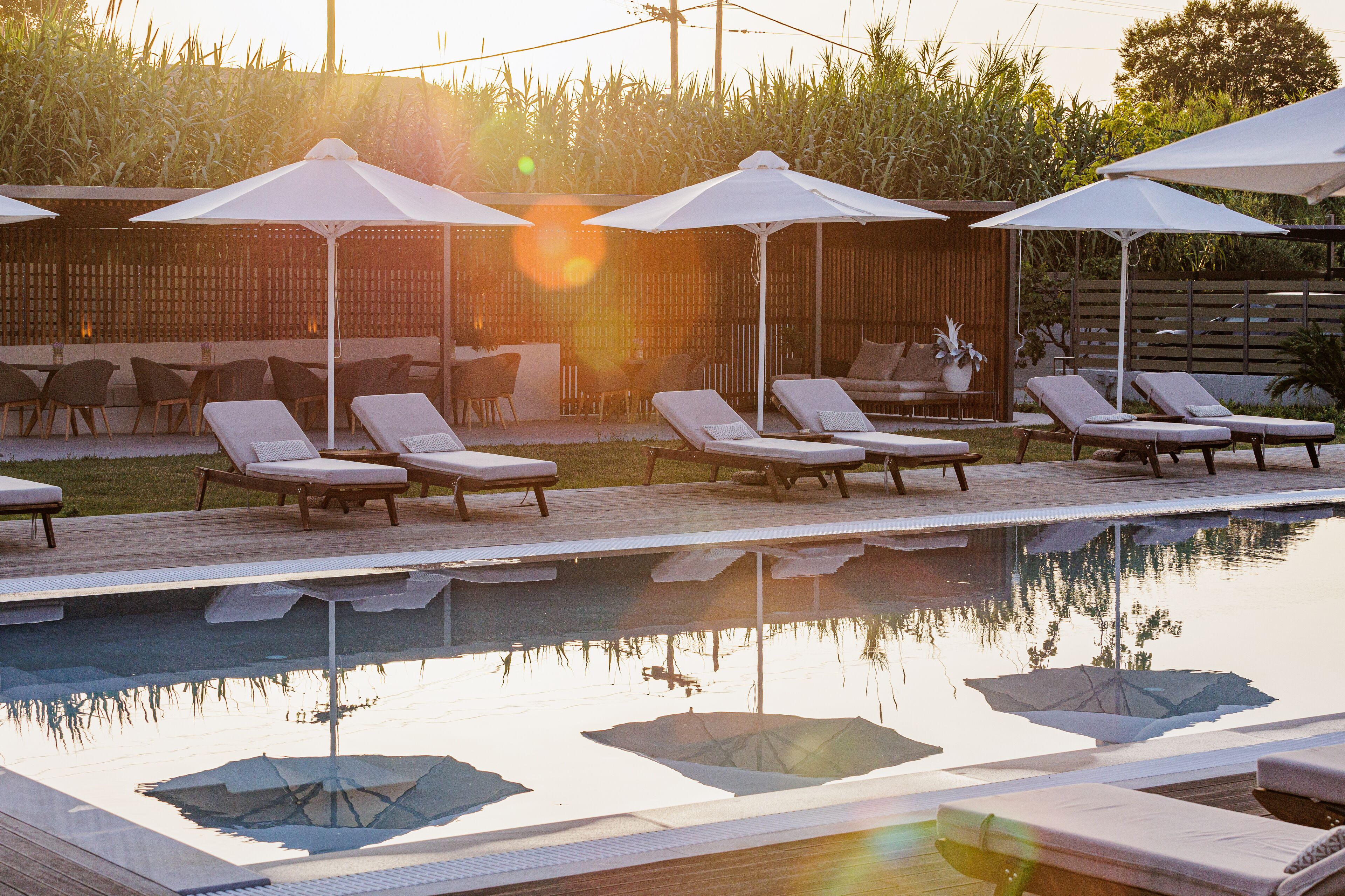 A pool area with lounge chairs and umbrellas, surrounded by a wooden deck and a bamboo fence.