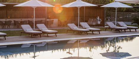 A pool area with lounge chairs and umbrellas, surrounded by a wooden deck and a bamboo fence.