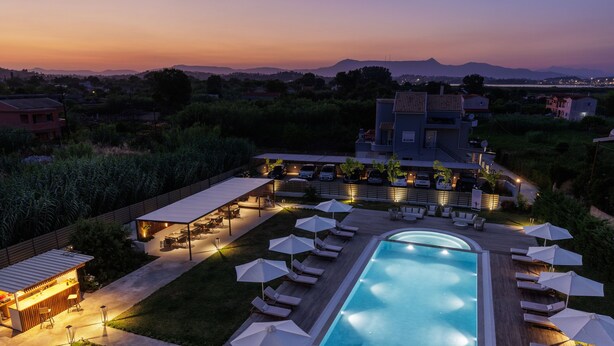 A swimming pool with lounge chairs and umbrellas, surrounded by a deck and a bar area. - V Luxury Suites (Corfu)