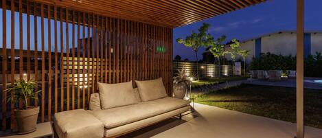A modern outdoor seating area with a wooden slatted ceiling, a beige sofa, and a potted plant.
