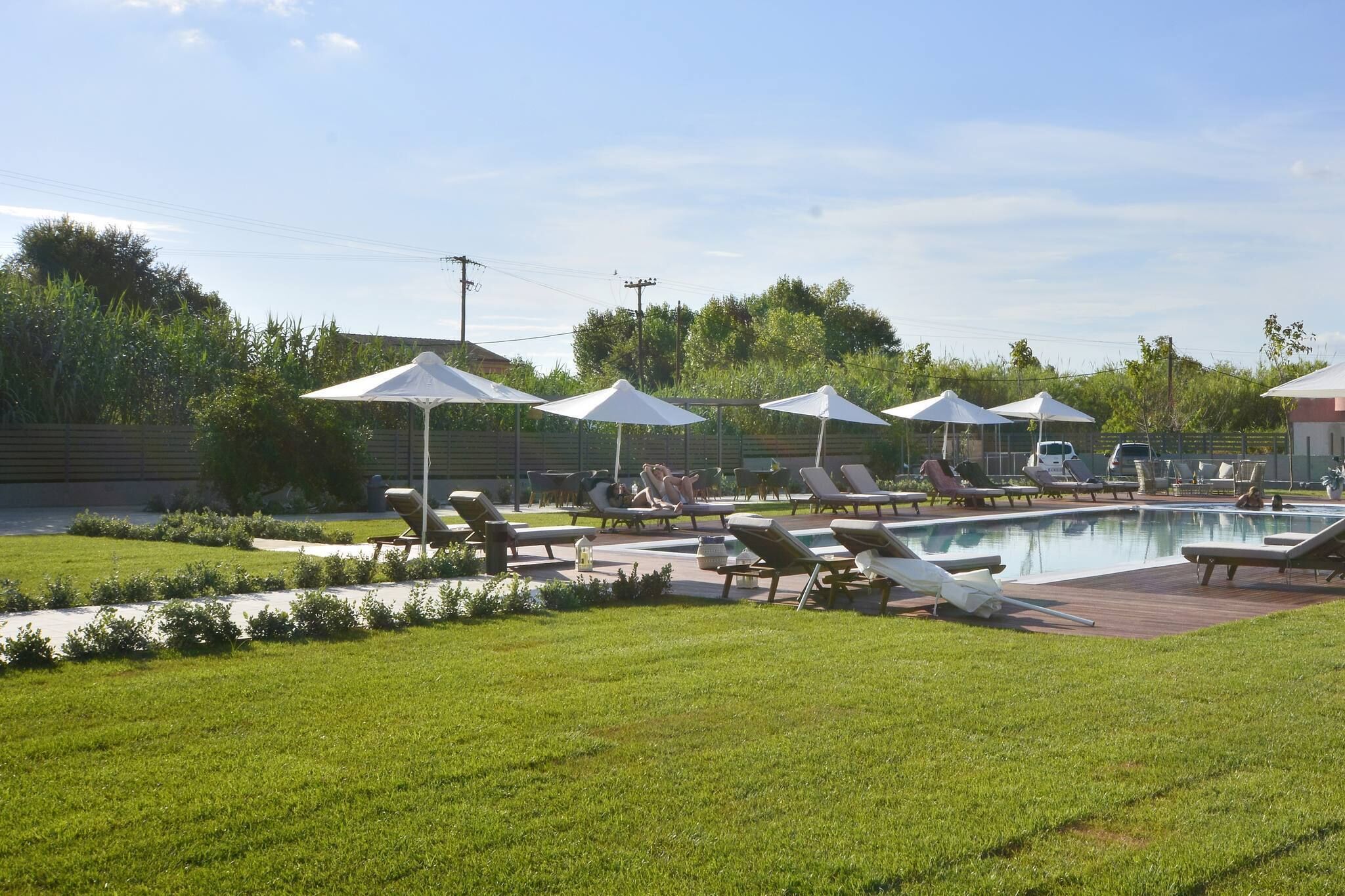 A poolside area with lounge chairs and umbrellas, surrounded by a well-maintained lawn and a wooden deck.
