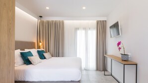 A modern bedroom with a large bed, a bedside table with a vase, and a TV mounted on the wall. - V Luxury Suites (Corfu)