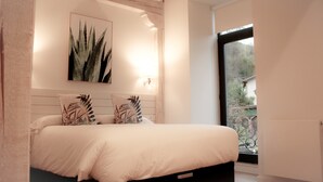 Een slaapkamer met een bed, een kunstwerk aan de muur en een raam met uitzicht op groen.
