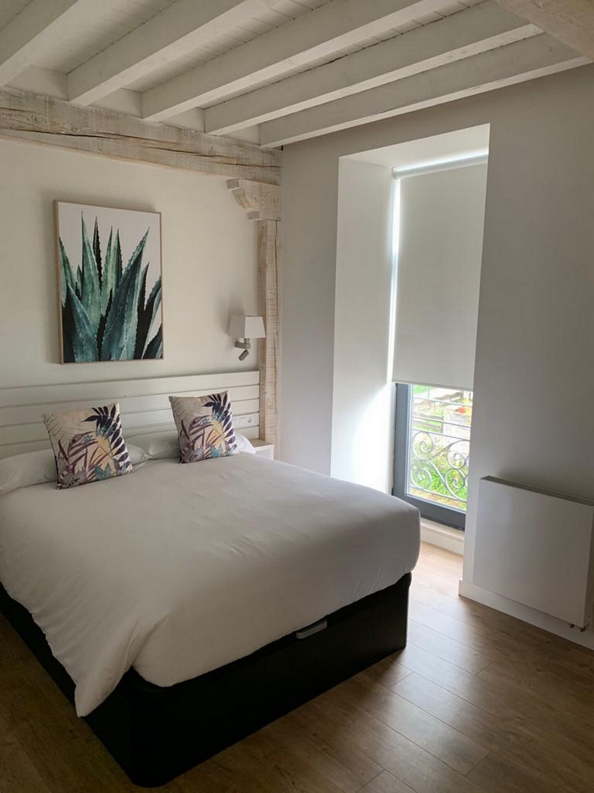 A bedroom with a large bed, a wall-mounted plant, and a window with a view of greenery.
