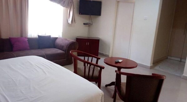 A hotel room with a bed, a small table with a chair, a television, and a wardrobe.