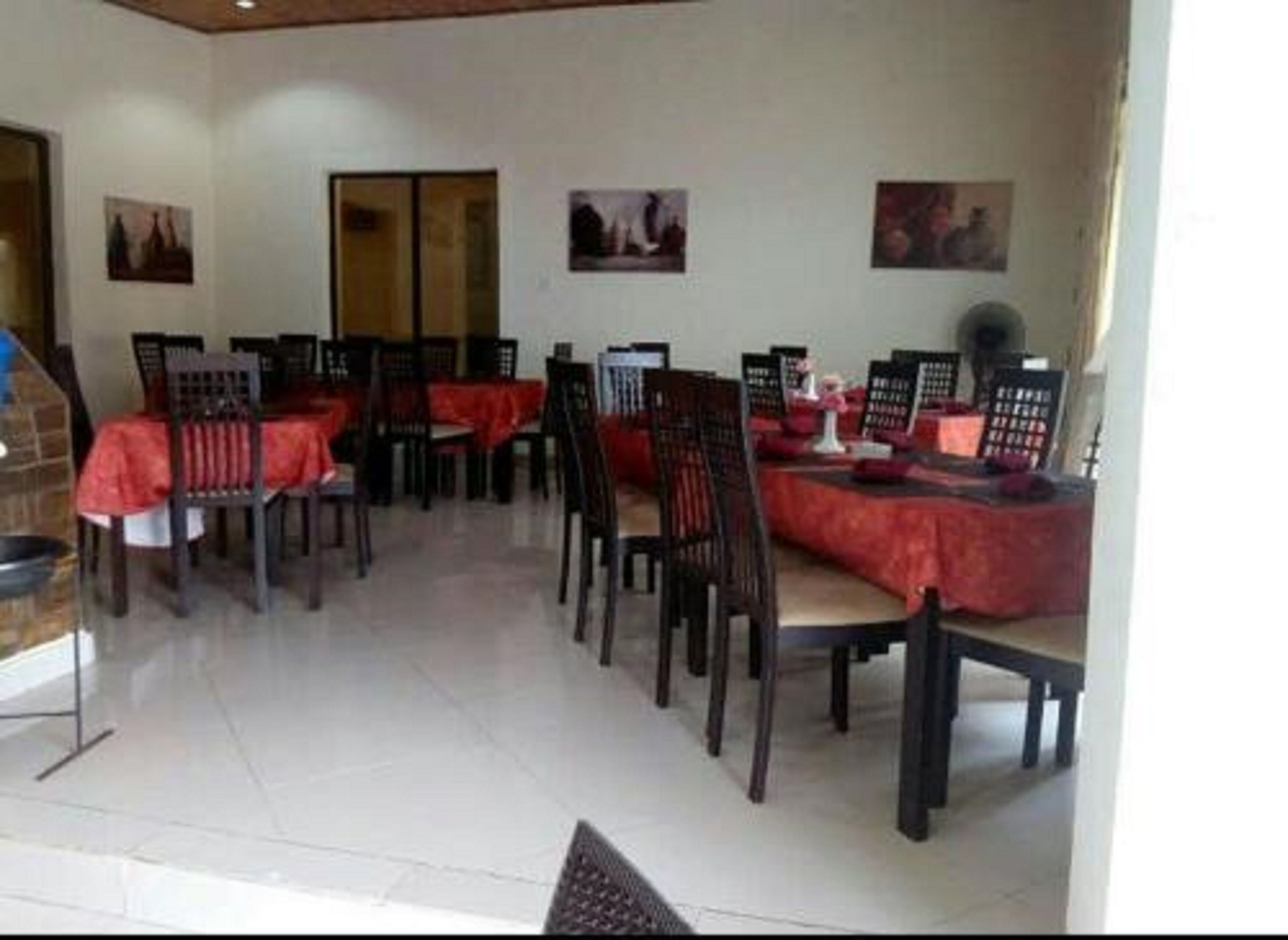 Un comedor con mesas y sillas, algunas con manteles rojos. Hay cuadros en las paredes.