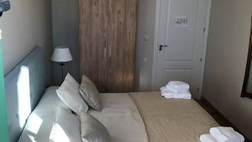 A hotel room with a bed, a wardrobe, a door with a sign, and a lamp.