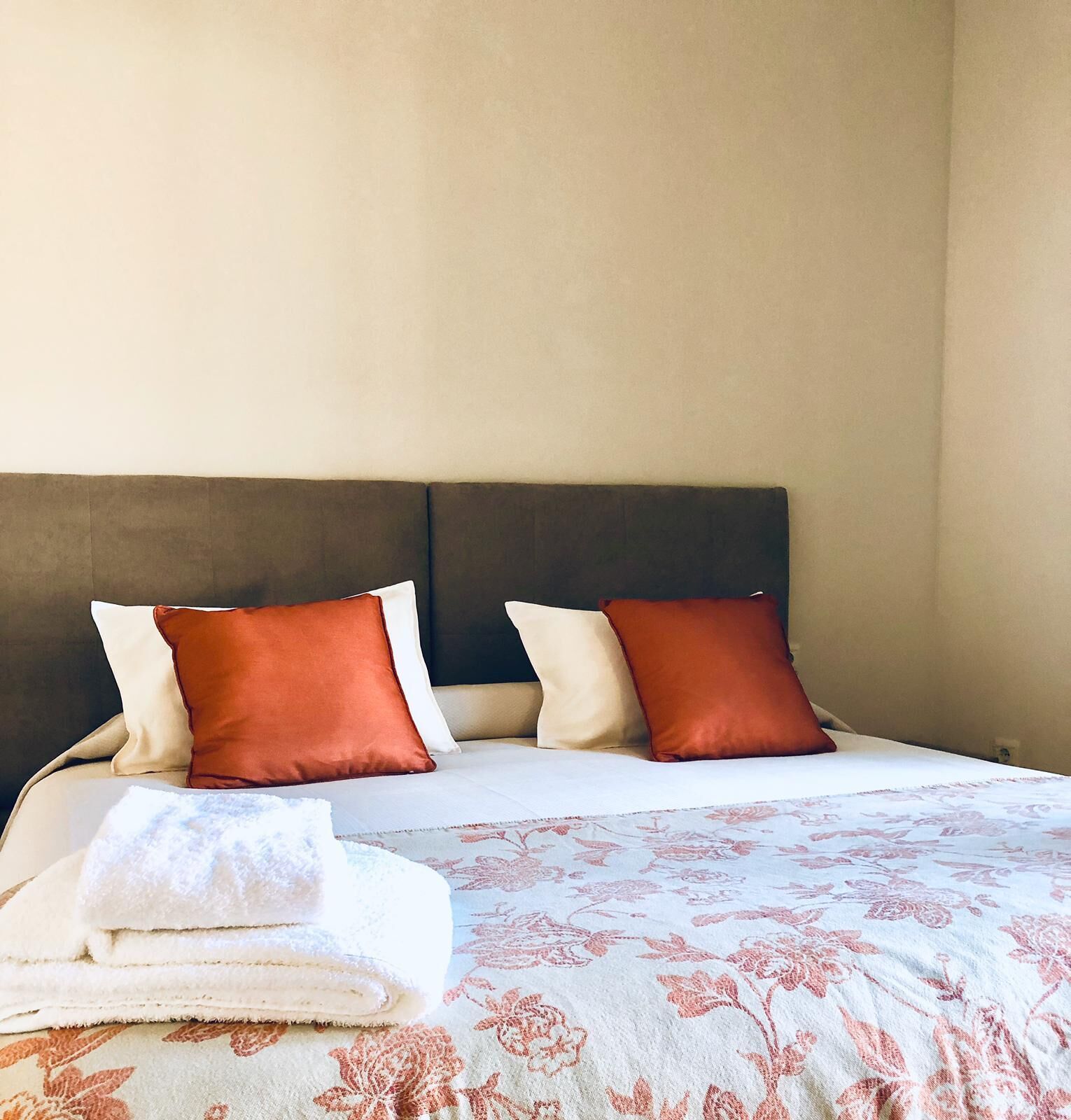 A bed with a floral-patterned bedspread and two pillows, one red and one white.