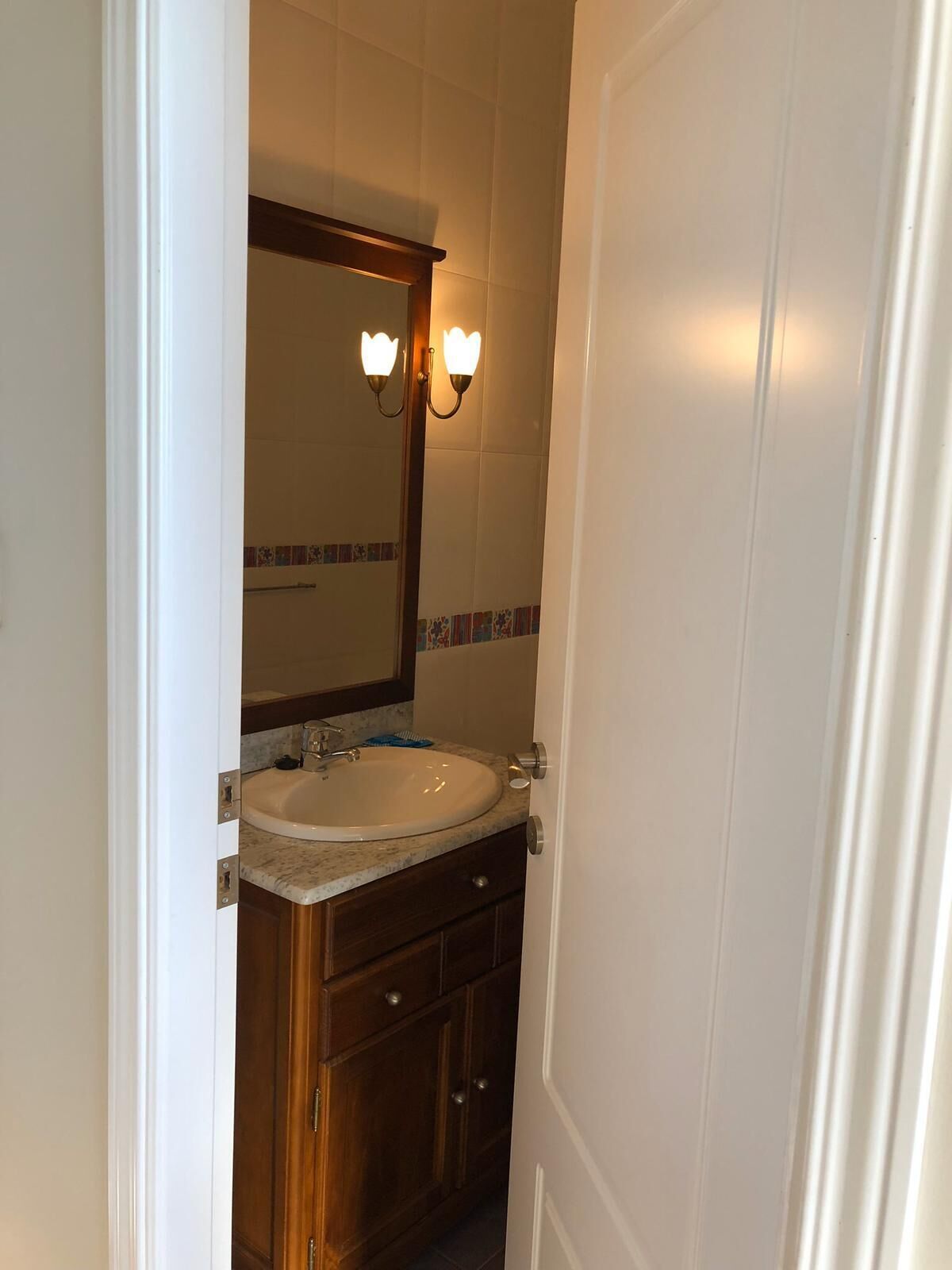 Un baño con lavamanos blanco, armarios de madera y un espejo con luces empotradas.