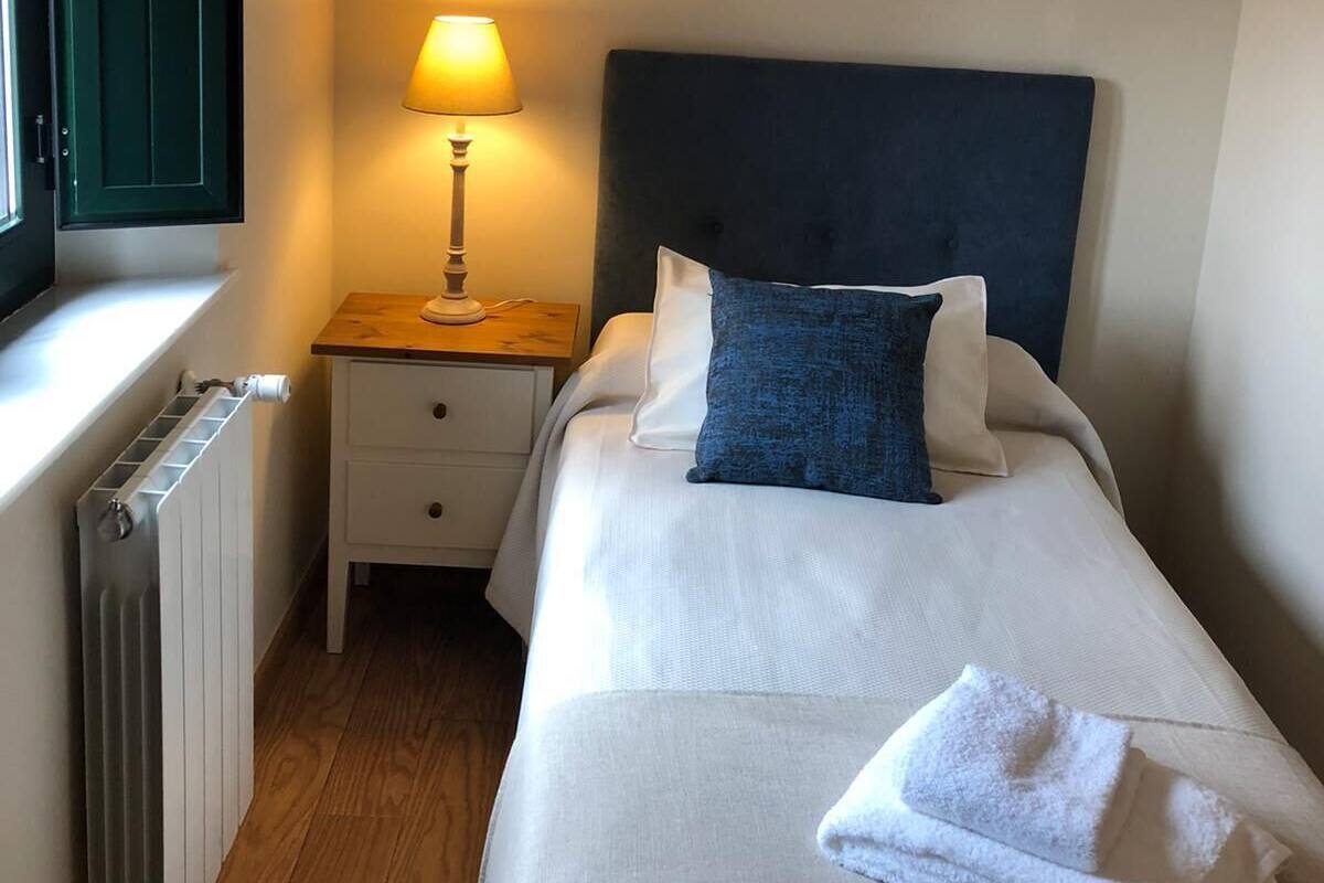 Ein ordentlich eingerichtetes Schlafzimmer mit einem Bett, einem Nachttisch mit Lampe, einem Heizkörper und einem Fenster mit geschlossenen Rollläden.
