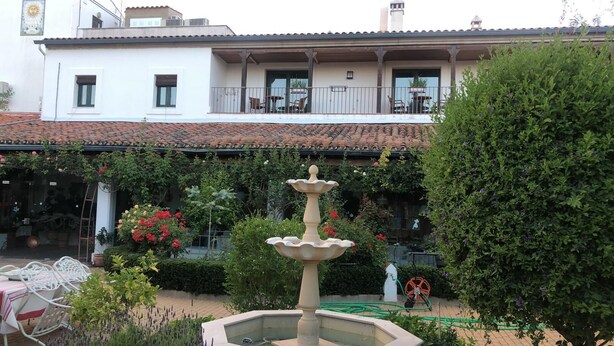 A courtyard with a fountain, outdoor seating, and a white building with a tiled roof. - Hotel La Muralla (Zafra)