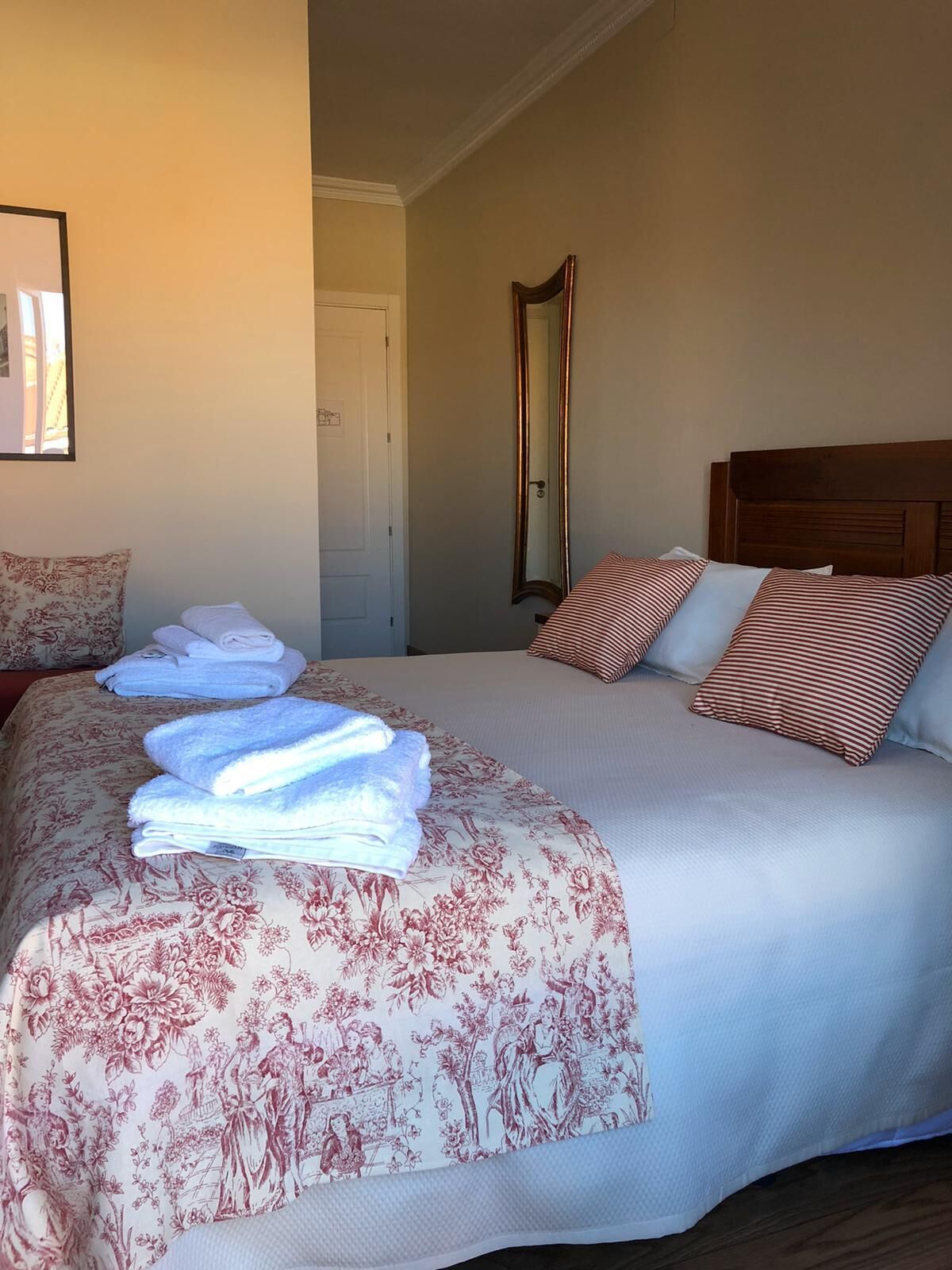 Una cama bien hecha con ropa de cama floral, un cabecero de madera y un espejo en la pared.
