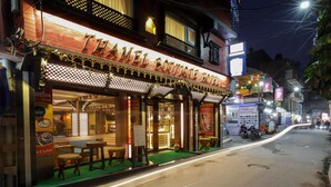 Um hotel chamado 'Theamel Boutique Hotel', com uma cafeteria visível e área de estar externa.