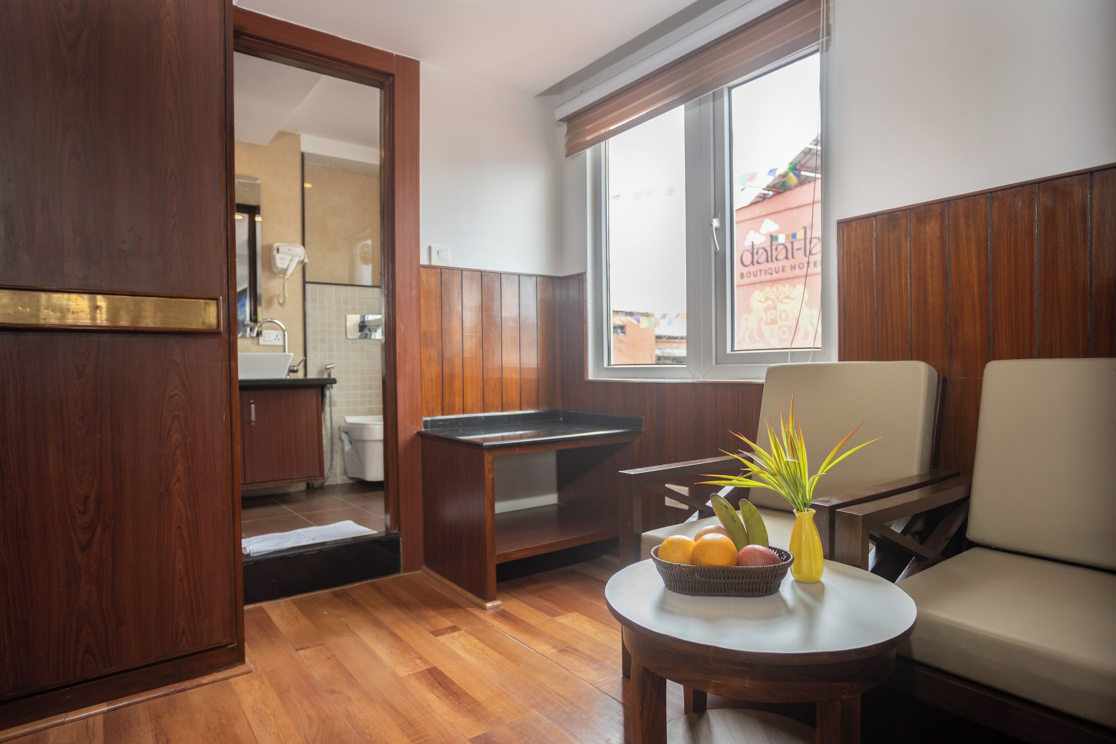 A room with a wooden floor, a dining table with a vase of flowers, a sofa, and a window with a view of the outside.