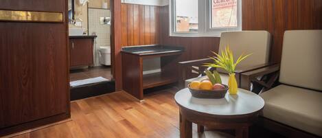 A room with a wooden floor, a dining table with a vase of flowers, a sofa, and a window with a view of the outside.
