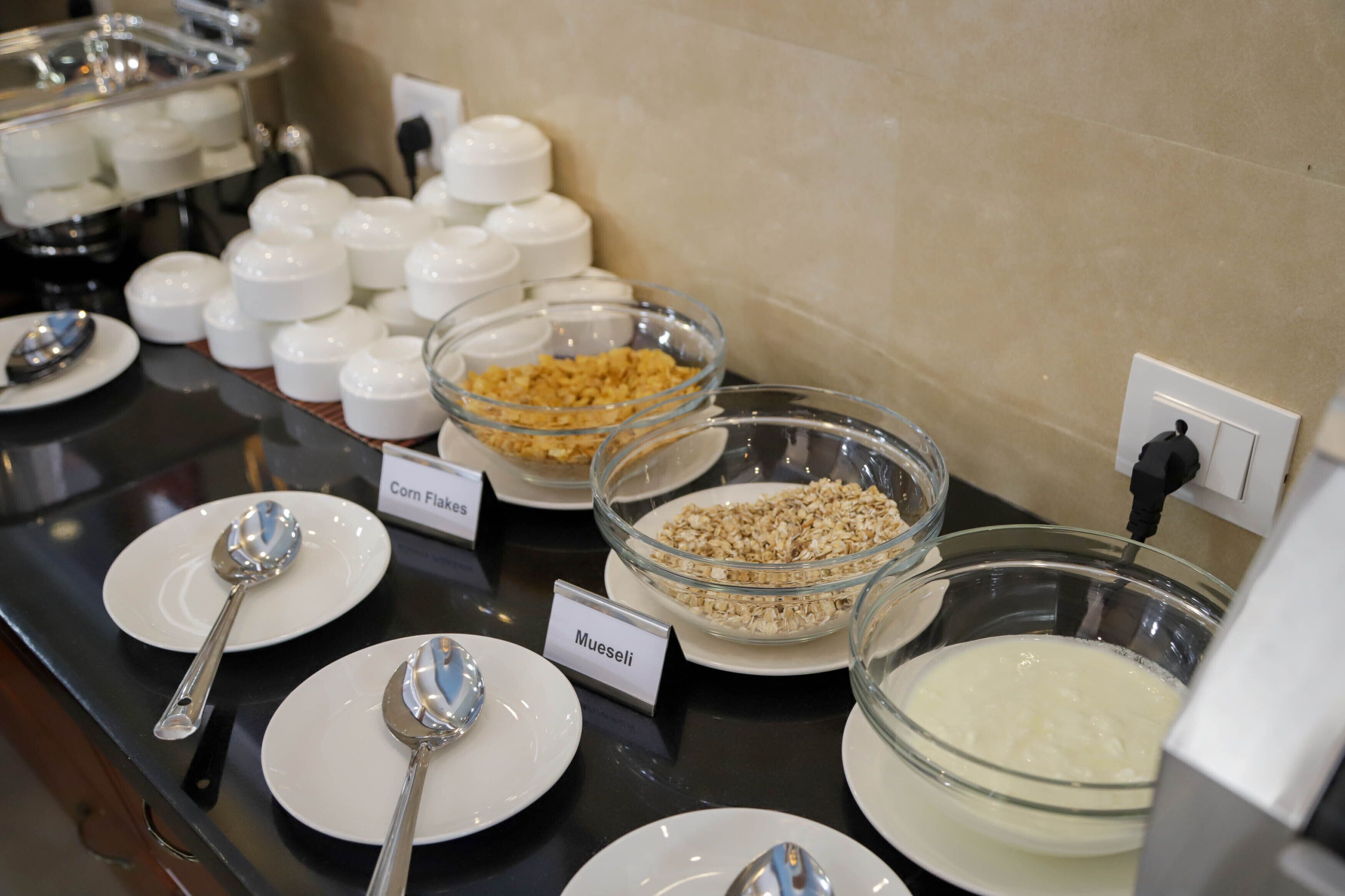 Een ontbijtbuffet met bakken vol cornflakes, muesli en yoghurt, duidelijk gelabeld.