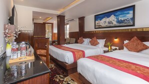 Quarto de hotel com duas camas, uma mesa com um vaso de flores e uma pintura de montanhas na parede.