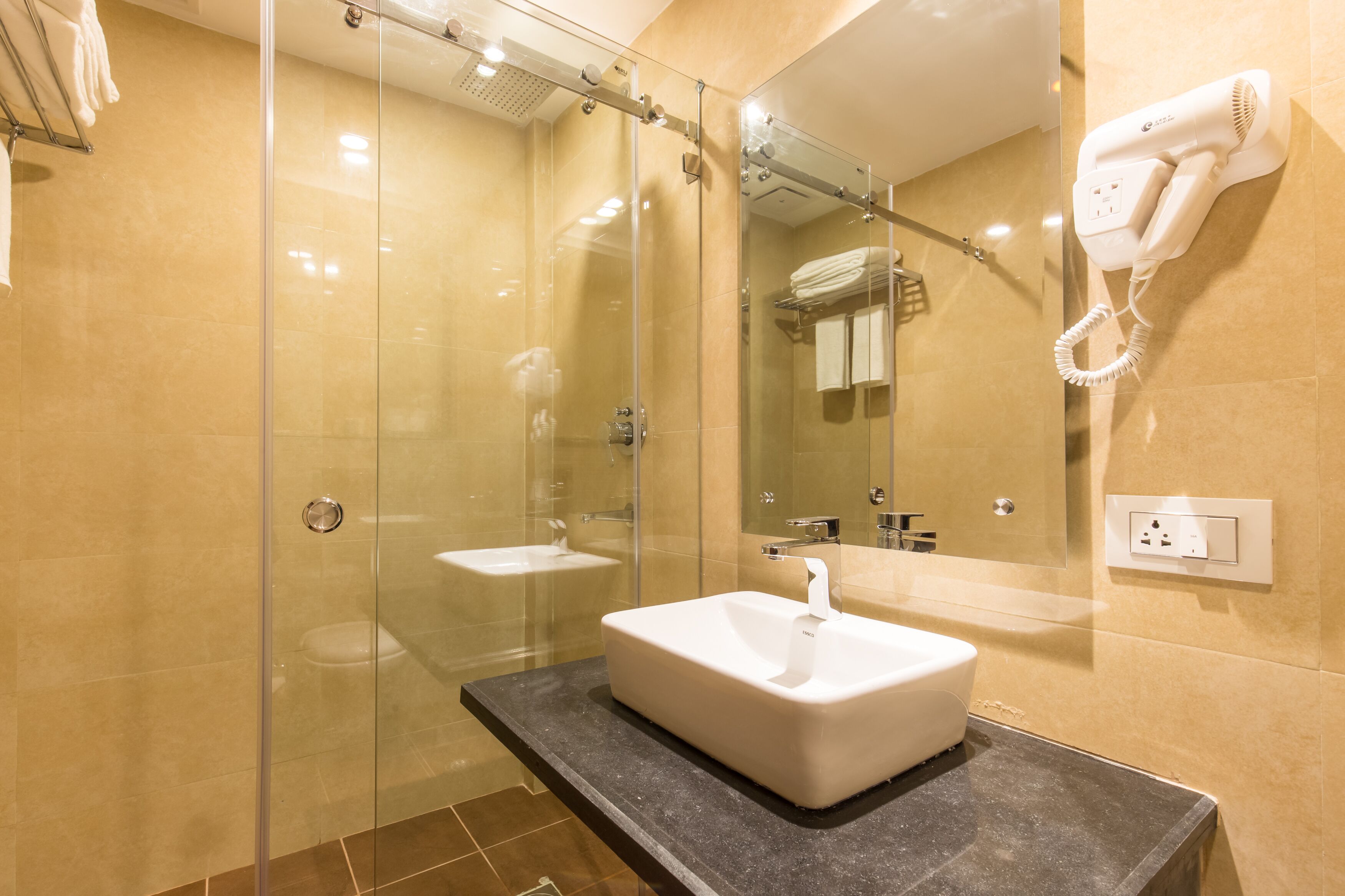 A modern bathroom with a glass-enclosed shower, a white sink, and a hairdryer mounted on the wall.