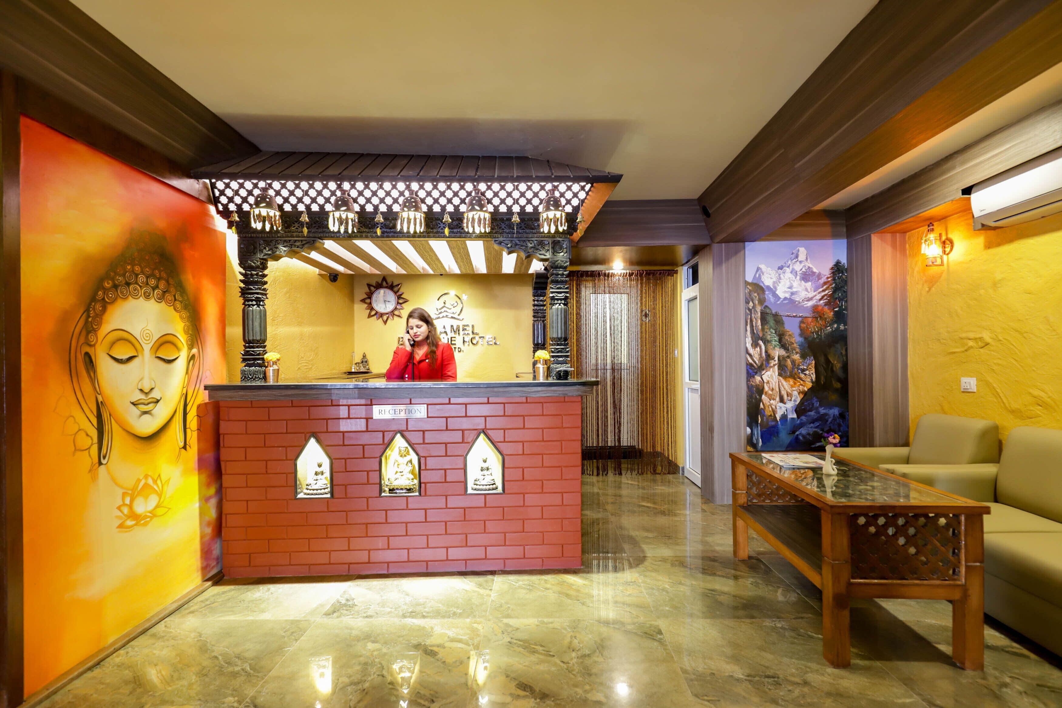 A hotel reception area with a red brick counter, a receptionist, and a large Buddha mural.