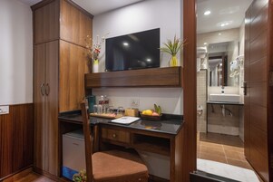 Cocina compacta con una TV integrada, armarios de madera, un refrigerador pequeño y una encimera con una cesta de fruta.