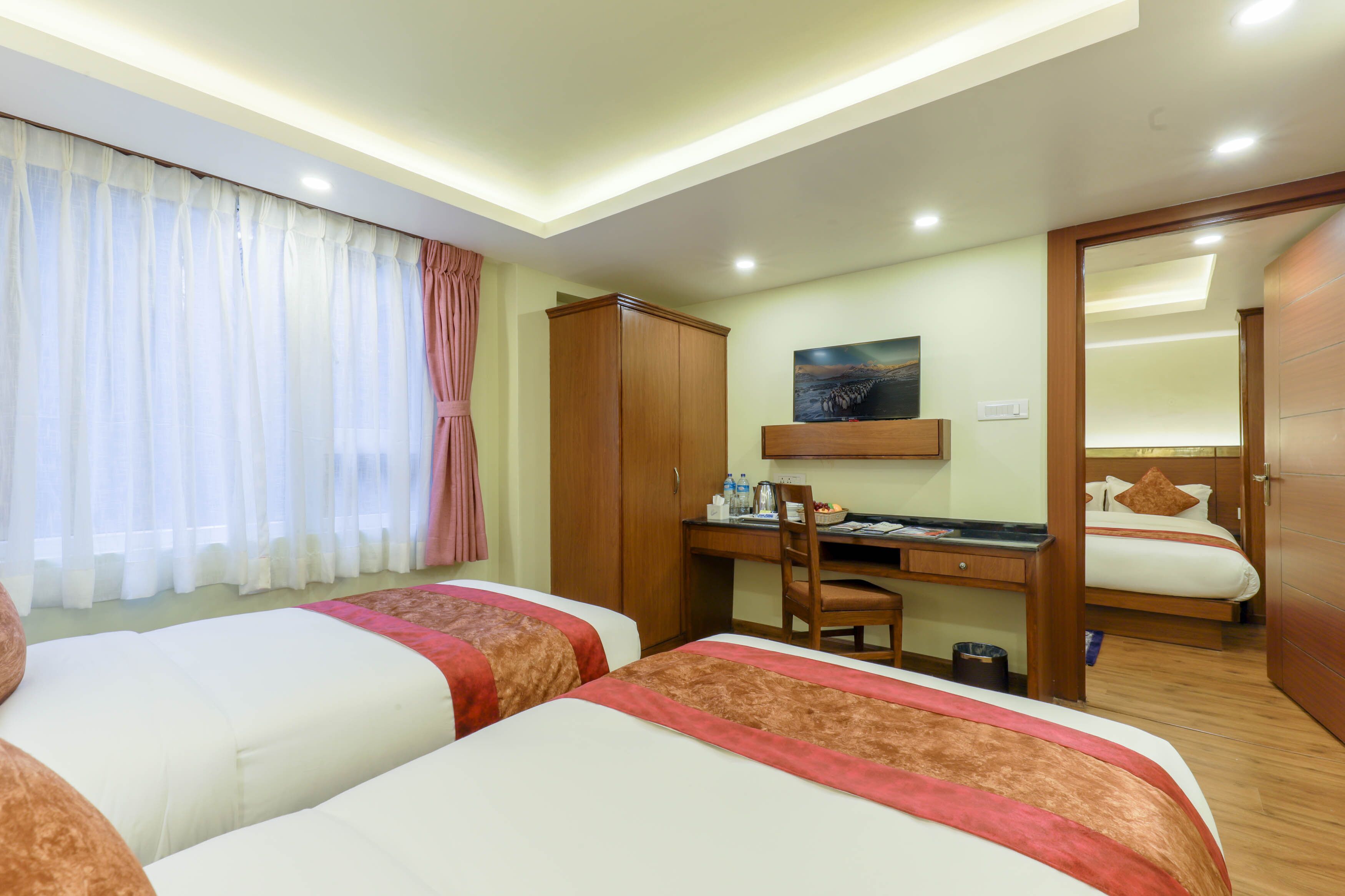 A hotel room with two beds, a desk with a chair, a wardrobe, and a painting on the wall.