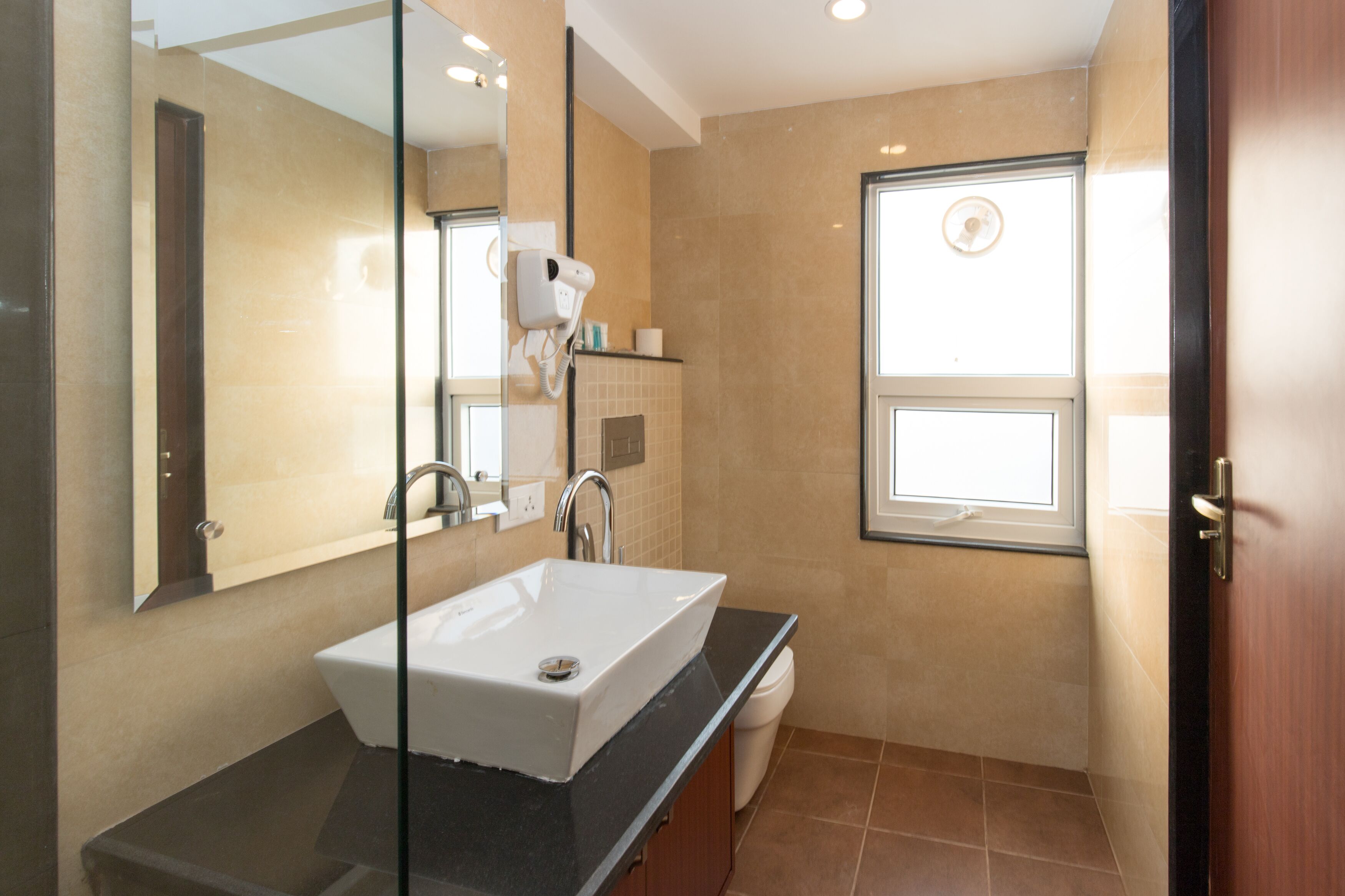 Un baño moderno con un espejo grande, un lavamanos blanco, un secador de pelo y una ventana.