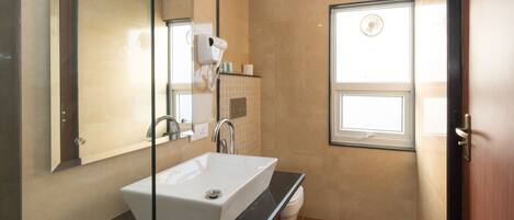 Un baño moderno con un espejo grande, un lavamanos blanco, un secador de pelo y una ventana.
