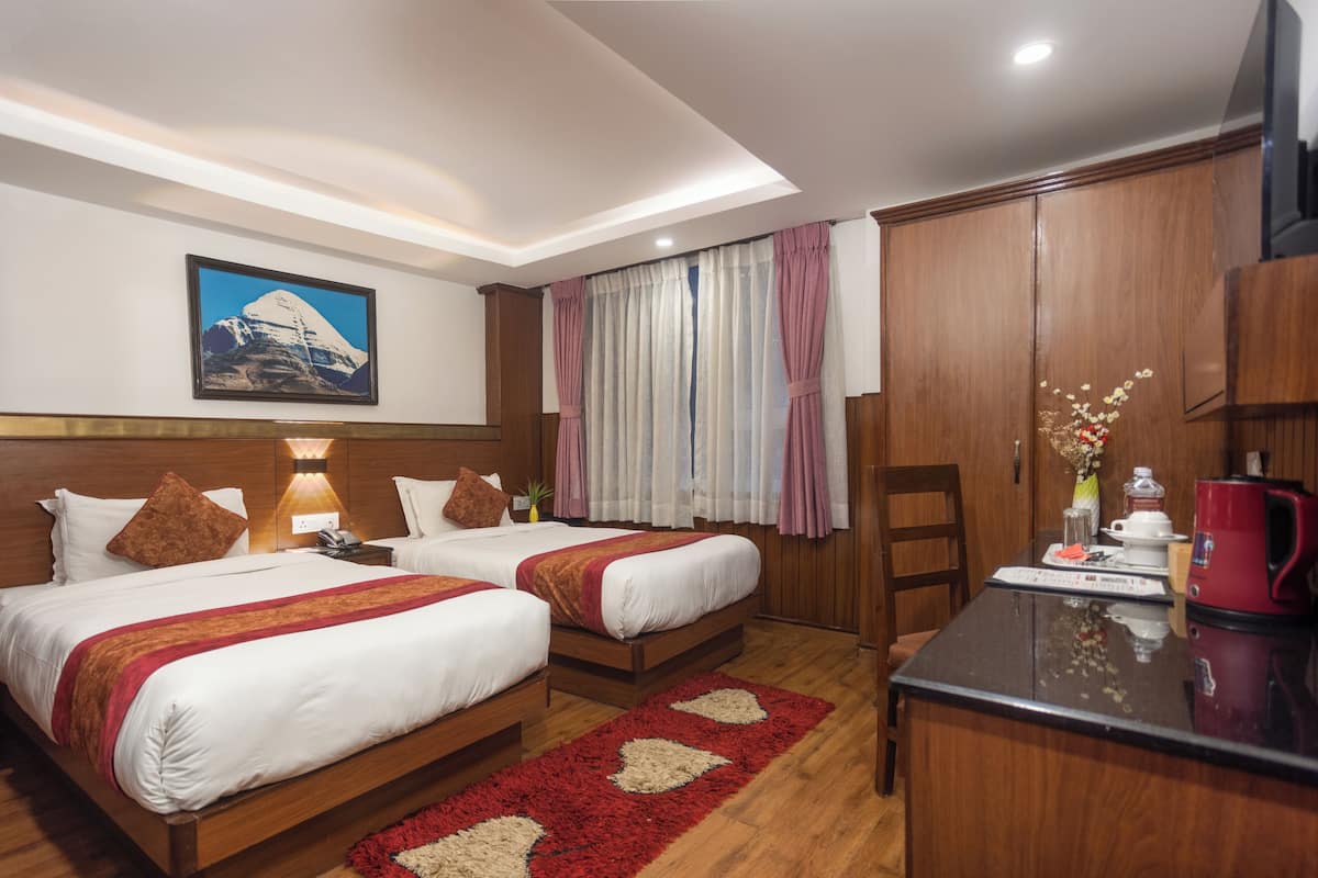 Ein Hotelzimmer mit zwei Betten, einem Holzschrank, einem Schreibtisch mit einem roten Wasserkocher und einem Berg-Gemälde an der Wand.