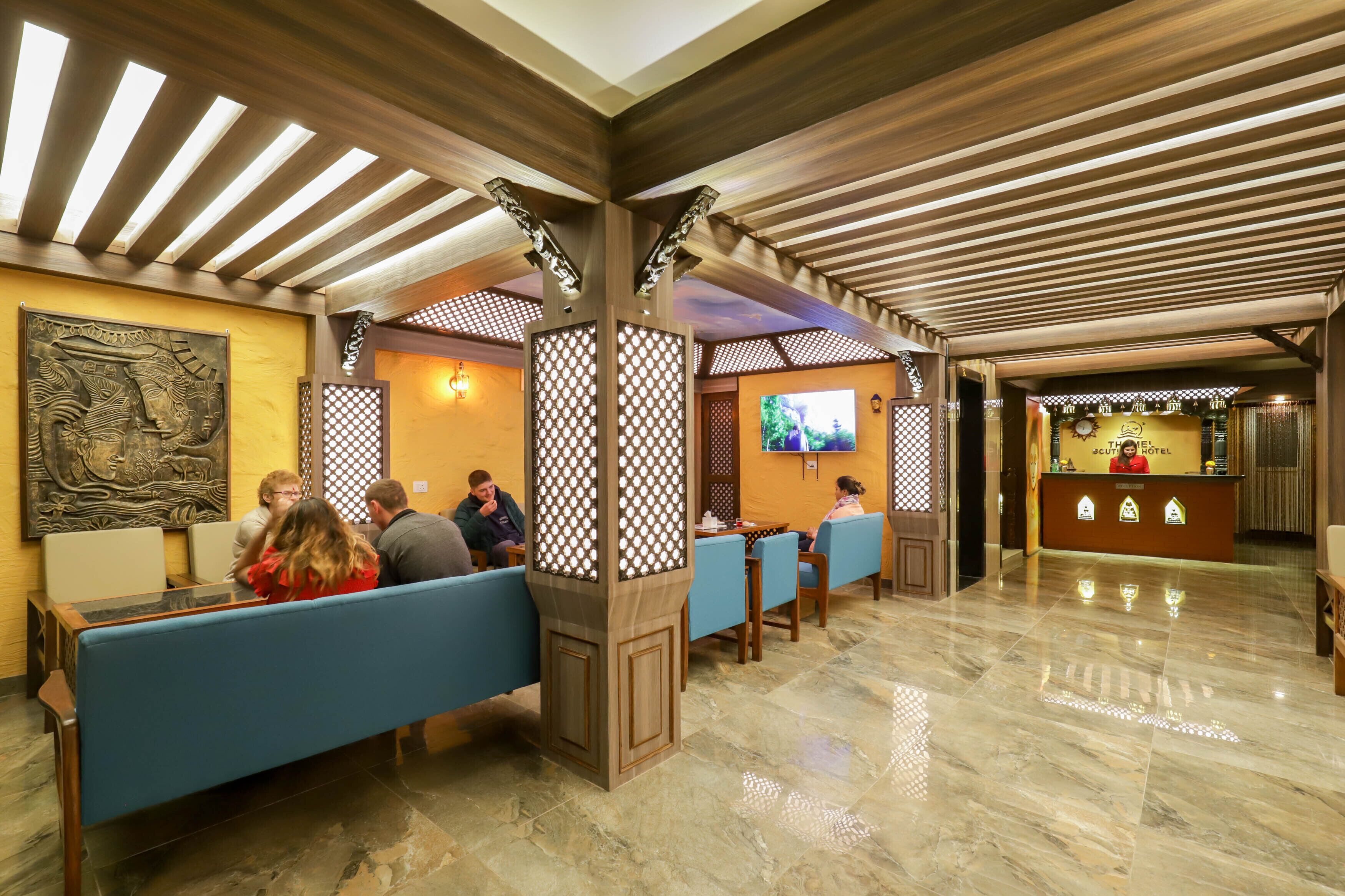 Un hall d’hôtel avec des poutres en bois, des sièges bleus, un comptoir d’accueil et un grand téléviseur fixé au mur.