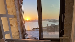 Quarto com uma cama grande, vista do pôr do sol sobre a água e uma parede de pedra.