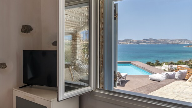 Quarto com televisão em móvel, ampla janela com vista para piscina e mar.