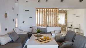 Uma sala de estar moderna com um sofá, uma mesa de centro com um tabuleiro de biscoitos e copos de suco de laranja, e uma parede de pedra ao fundo.