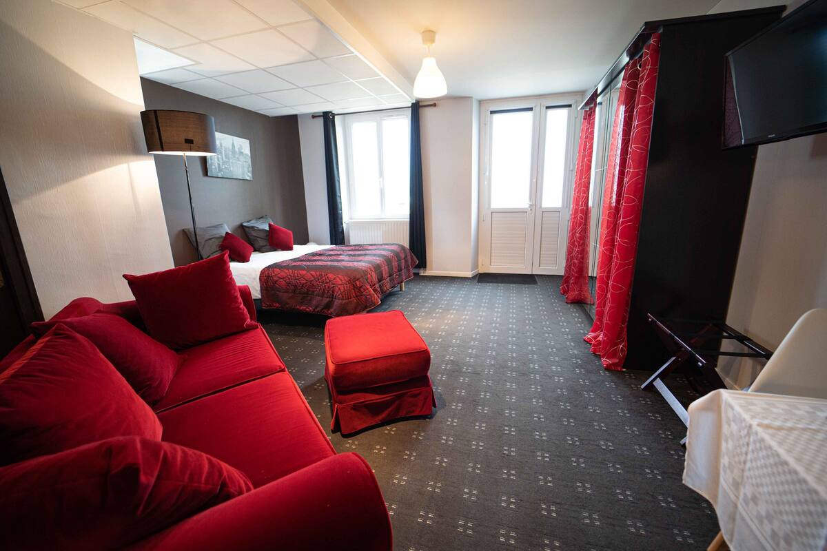Ein Hotelzimmer mit rotem Sofa, einem Bett mit roter Bettwäsche, einem Fernseher und einem Fenster mit Vorhängen.