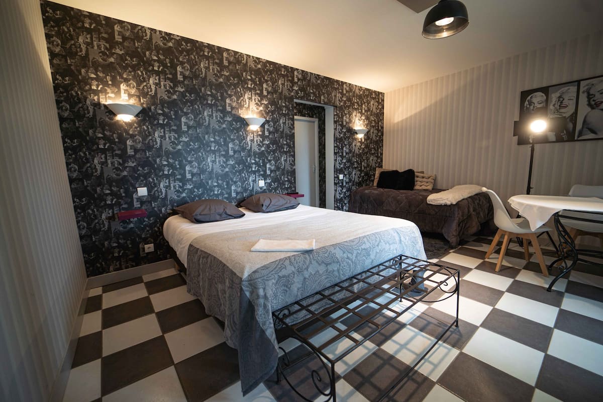 Ein Schlafzimmer mit Schachbrettmuster-Boden, einem Bett mit gemustertem Überwurf, zwei Wandleuchten und einer Tür.